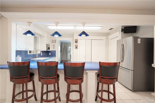 kitchen featuring light tile patterned floors, visible vents, a breakfast bar area, freestanding refrigerator, and a peninsula