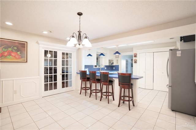 kitchen with light tile patterned floors, a wainscoted wall, a breakfast bar, freestanding refrigerator, and a peninsula