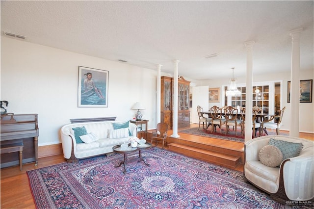 living area with decorative columns, baseboards, visible vents, wood finished floors, and a textured ceiling