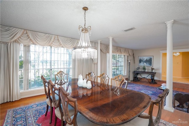 dining area with a chandelier, decorative columns, a textured ceiling, and wood finished floors