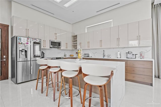 kitchen with a breakfast bar area, white cabinetry, appliances with stainless steel finishes, a kitchen island, and backsplash