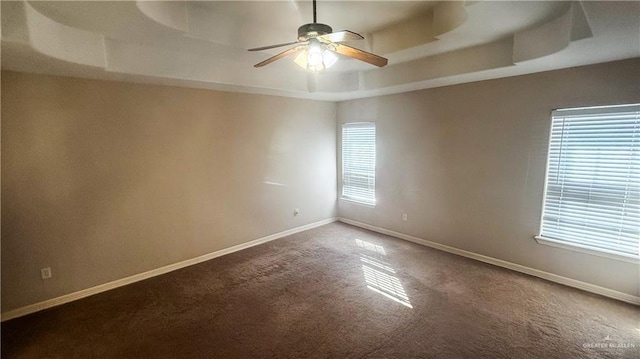 empty room featuring dark carpet, a raised ceiling, ceiling fan, and baseboards