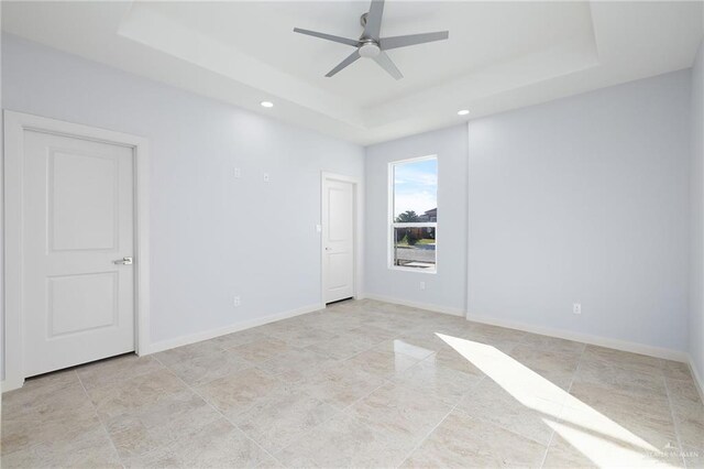 unfurnished room with a raised ceiling, a ceiling fan, and baseboards