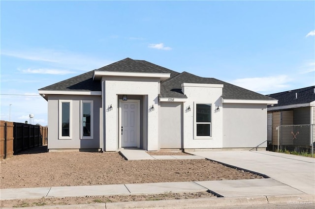 view of front of house with roof with shingles, fence, driveway, and stucco siding