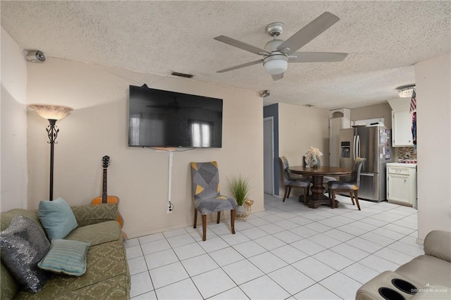 living room with light tile patterned floors, ceiling fan, visible vents, and a textured ceiling