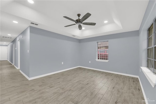 empty room featuring ceiling fan, a raised ceiling, and light wood-type flooring