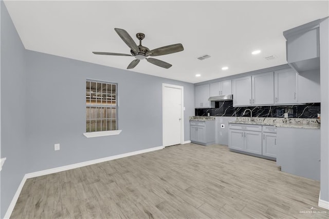 kitchen with light stone countertops, sink, ceiling fan, backsplash, and light hardwood / wood-style floors