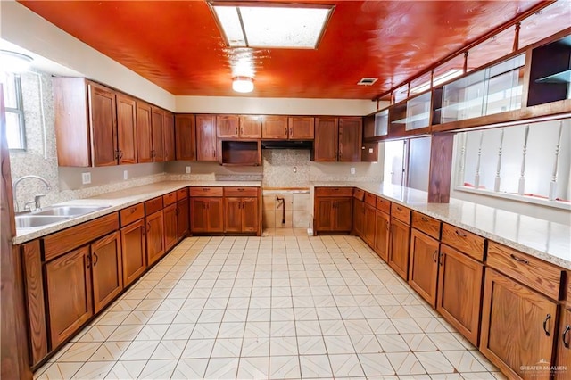 kitchen featuring decorative backsplash, brown cabinets, a skylight, and a sink