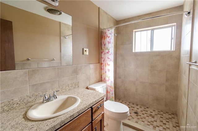 full bathroom featuring a tile shower, toilet, tile walls, and vanity