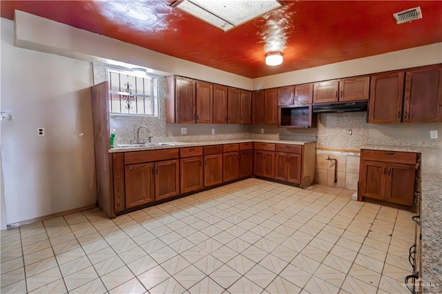 kitchen featuring under cabinet range hood, decorative backsplash, brown cabinetry, and a sink