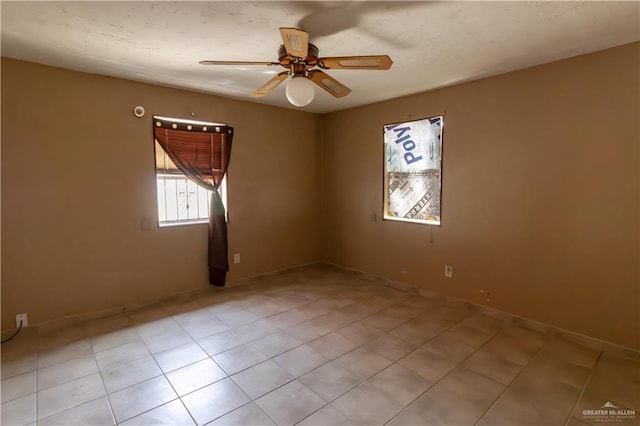 empty room with light tile patterned floors, baseboards, and a ceiling fan