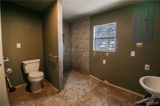 full bath featuring baseboards, toilet, electric panel, a tile shower, and a sink