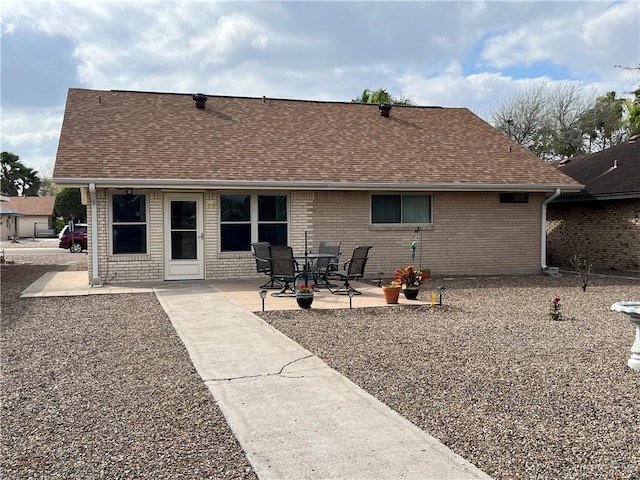 rear view of property featuring a shingled roof, a patio area, and brick siding