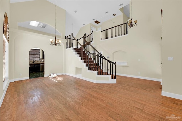 unfurnished living room featuring a chandelier, sink, hardwood / wood-style flooring, and a towering ceiling