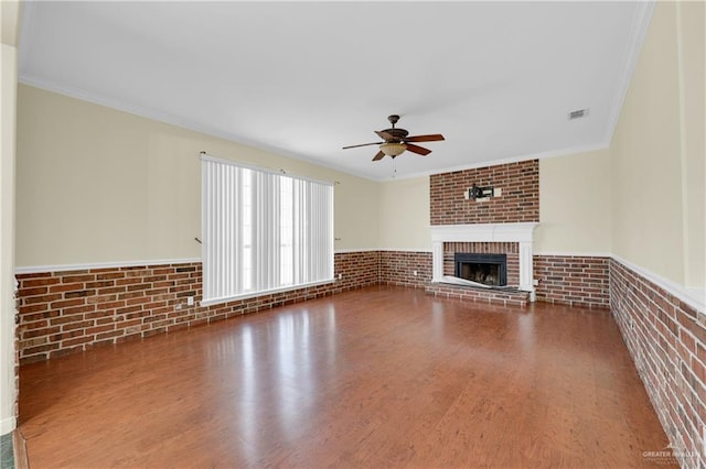 unfurnished living room with a brick fireplace, crown molding, hardwood / wood-style floors, and brick wall