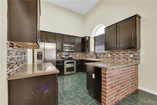 kitchen with dark brown cabinetry, stainless steel appliances, light stone countertops, decorative backsplash, and sink