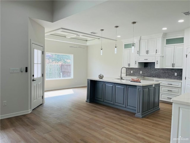 kitchen featuring pendant lighting, white cabinetry, an island with sink, sink, and light hardwood / wood-style flooring