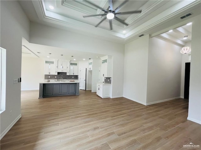 unfurnished living room featuring ceiling fan, a tray ceiling, light wood-type flooring, crown molding, and sink