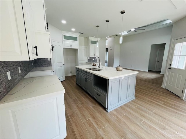 kitchen with pendant lighting, sink, an island with sink, gray cabinetry, and white cabinets