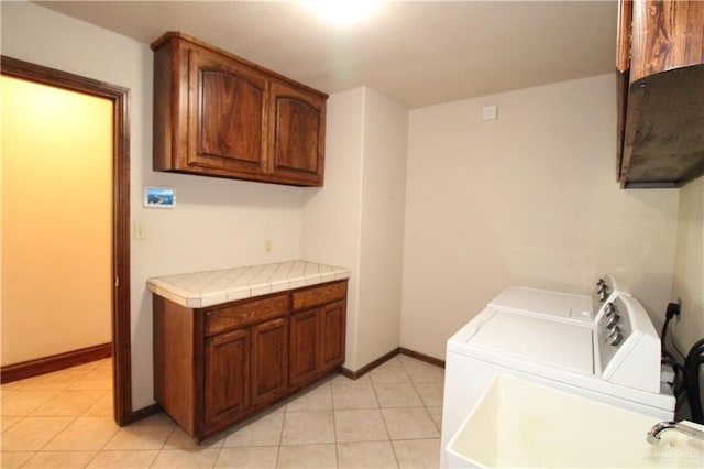 laundry area featuring washing machine and dryer, light tile patterned floors, and cabinets