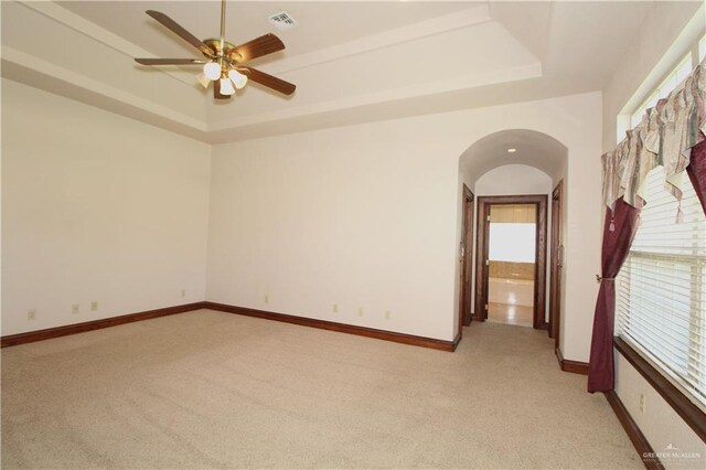 carpeted empty room with ceiling fan, a healthy amount of sunlight, and a tray ceiling