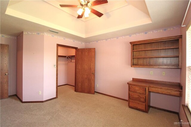 unfurnished office with a tray ceiling, ceiling fan, and light colored carpet