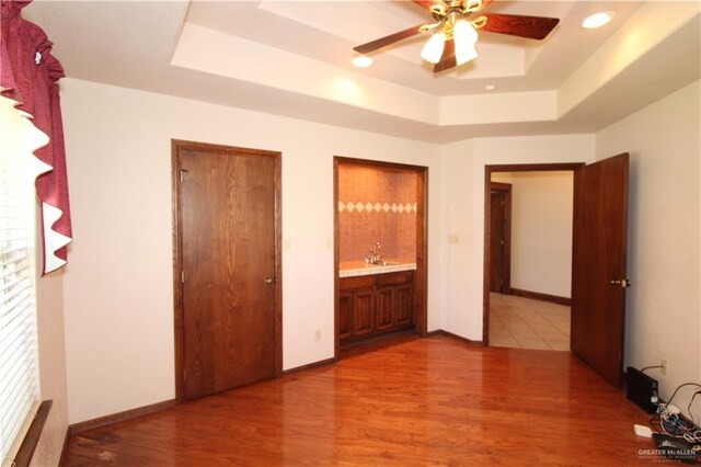 unfurnished bedroom with a raised ceiling, sink, hardwood / wood-style flooring, ceiling fan, and connected bathroom