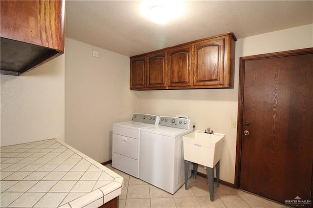 clothes washing area featuring washer and dryer, light tile patterned floors, and cabinets