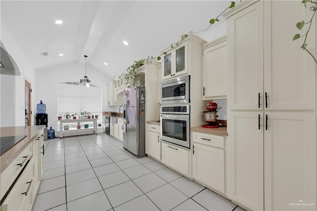 kitchen featuring light tile patterned flooring, vaulted ceiling with beams, appliances with stainless steel finishes, decorative backsplash, and cream cabinetry