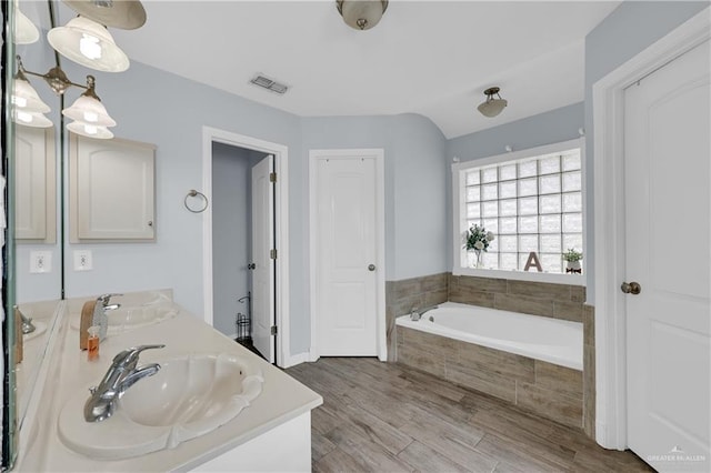 bathroom with vanity, wood-type flooring, and tiled tub