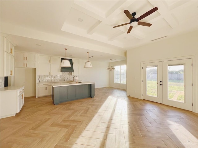 kitchen featuring coffered ceiling, sink, decorative light fixtures, a center island with sink, and white cabinets