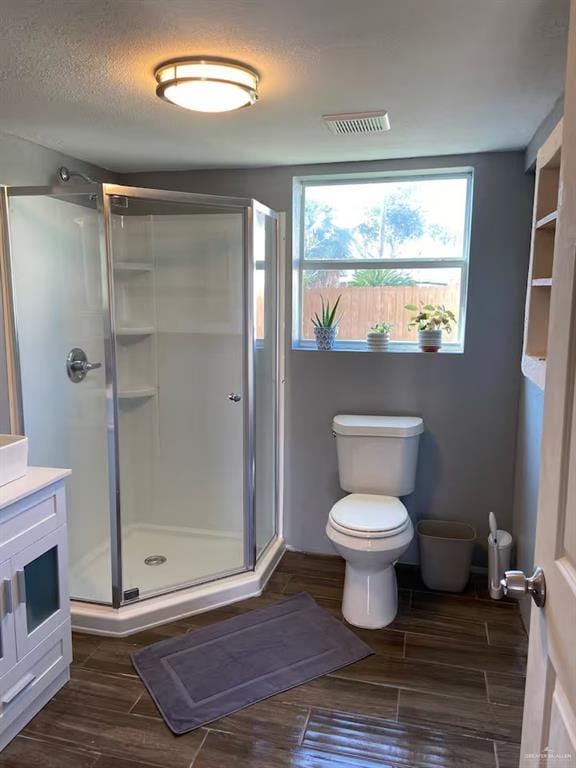 bathroom with a textured ceiling, vanity, toilet, and walk in shower