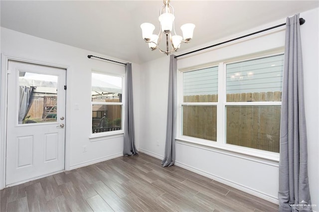 unfurnished dining area featuring a chandelier, baseboards, and wood finished floors