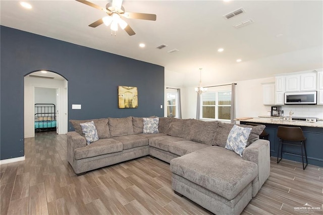 living room with arched walkways, light wood finished floors, visible vents, baseboards, and ceiling fan with notable chandelier