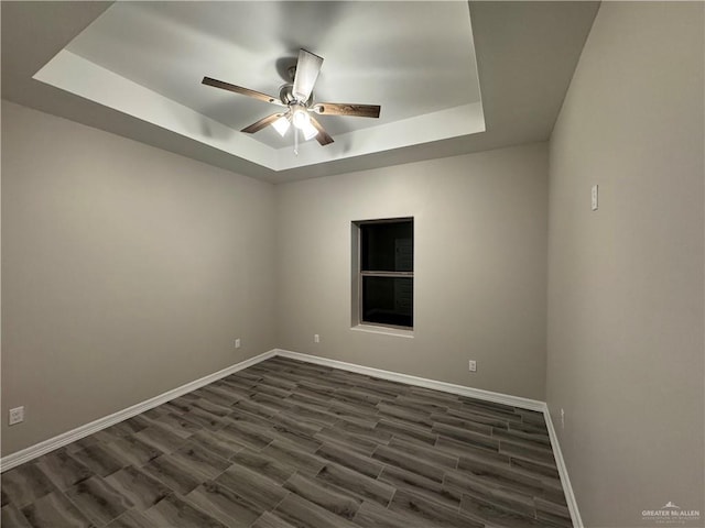 empty room featuring a raised ceiling, dark hardwood / wood-style floors, and ceiling fan