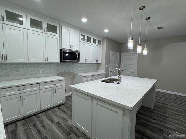 kitchen with pendant lighting, sink, white cabinets, dark wood-type flooring, and a center island with sink