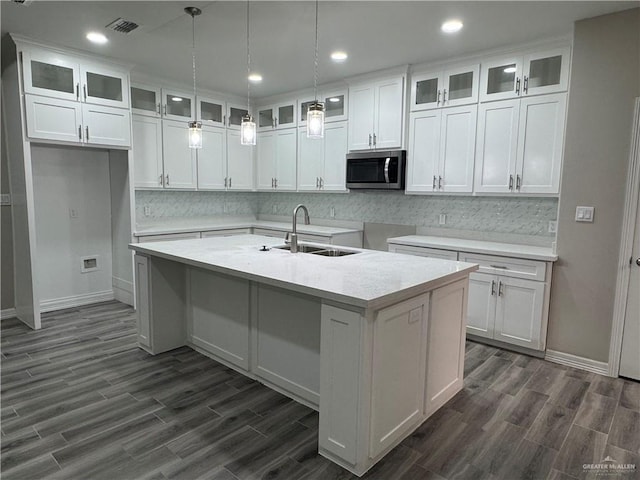 kitchen featuring white cabinetry, an island with sink, sink, decorative backsplash, and hanging light fixtures