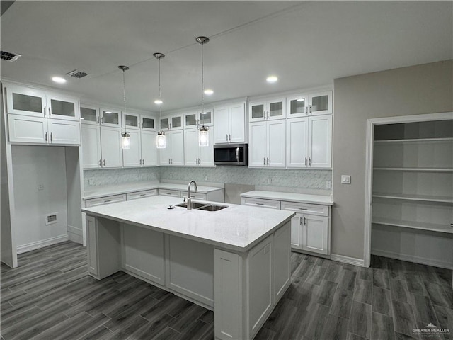 kitchen with tasteful backsplash, white cabinetry, sink, dark hardwood / wood-style flooring, and a center island with sink