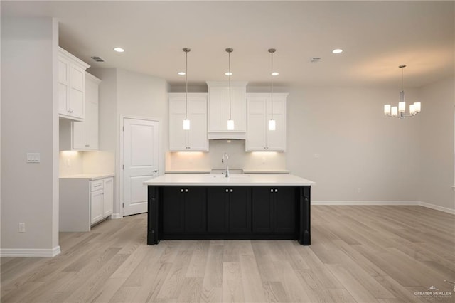 kitchen featuring decorative light fixtures, white cabinetry, an island with sink, and light hardwood / wood-style flooring