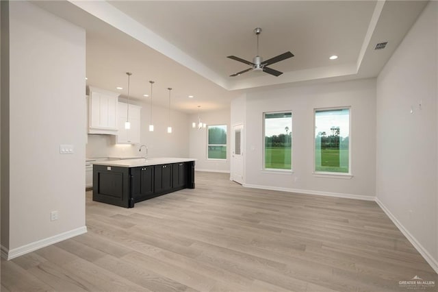 unfurnished living room with a tray ceiling, light hardwood / wood-style flooring, ceiling fan with notable chandelier, and sink