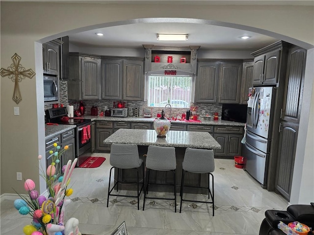 kitchen with sink, a breakfast bar, appliances with stainless steel finishes, a center island, and light stone counters