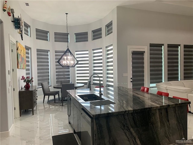 kitchen featuring a towering ceiling, sink, dark stone countertops, hanging light fixtures, and an island with sink