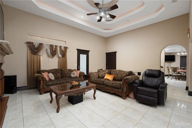 living room with a tray ceiling, ceiling fan, light tile patterned flooring, and a high ceiling