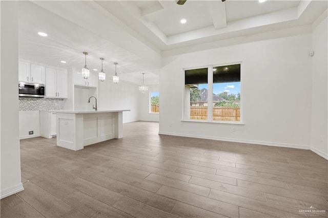 kitchen featuring pendant lighting, light hardwood / wood-style flooring, backsplash, an island with sink, and white cabinets