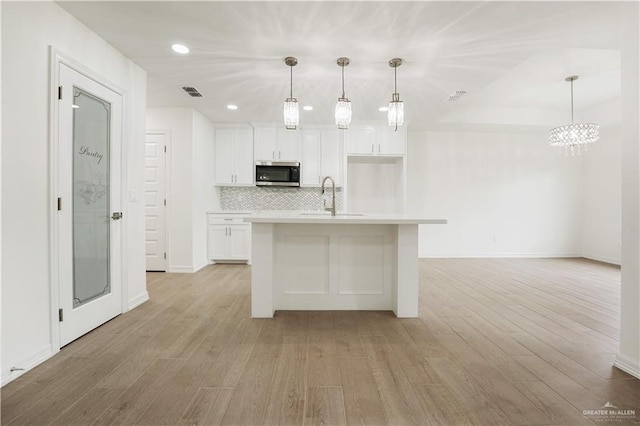 kitchen with an island with sink, sink, white cabinets, and decorative light fixtures