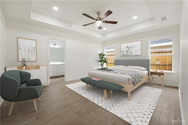 bedroom featuring hardwood / wood-style floors, a tray ceiling, ensuite bath, and ceiling fan