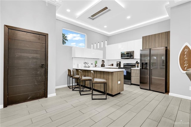 kitchen with white cabinetry, a kitchen breakfast bar, kitchen peninsula, light hardwood / wood-style floors, and appliances with stainless steel finishes