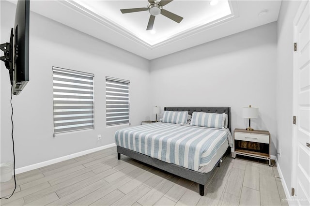 bedroom featuring ceiling fan, light wood-type flooring, and a tray ceiling