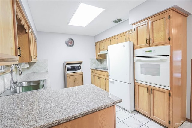 kitchen featuring a skylight, tasteful backsplash, white appliances, sink, and light tile patterned flooring