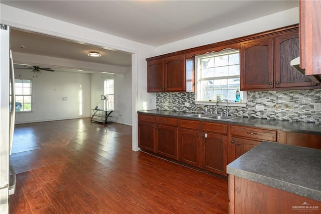 kitchen featuring dark countertops, dark wood finished floors, a sink, and decorative backsplash